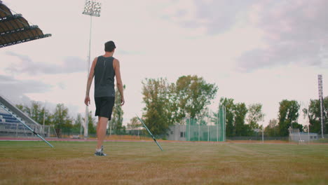 A-javelin-Thrower-walks-around-the-stadium-with-spears-and-collects-them.-Go-with-a-spear-in-hand-against-the-background-of-the-stadium-stands.-The-training-of-the-Olympic-champion.